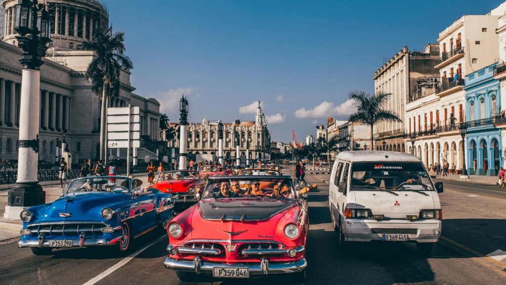 Colorful vintage cars driving by iconic buildings in Havana, Cuba.